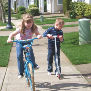 Laurel and Brent riding their bike and scooter outside.